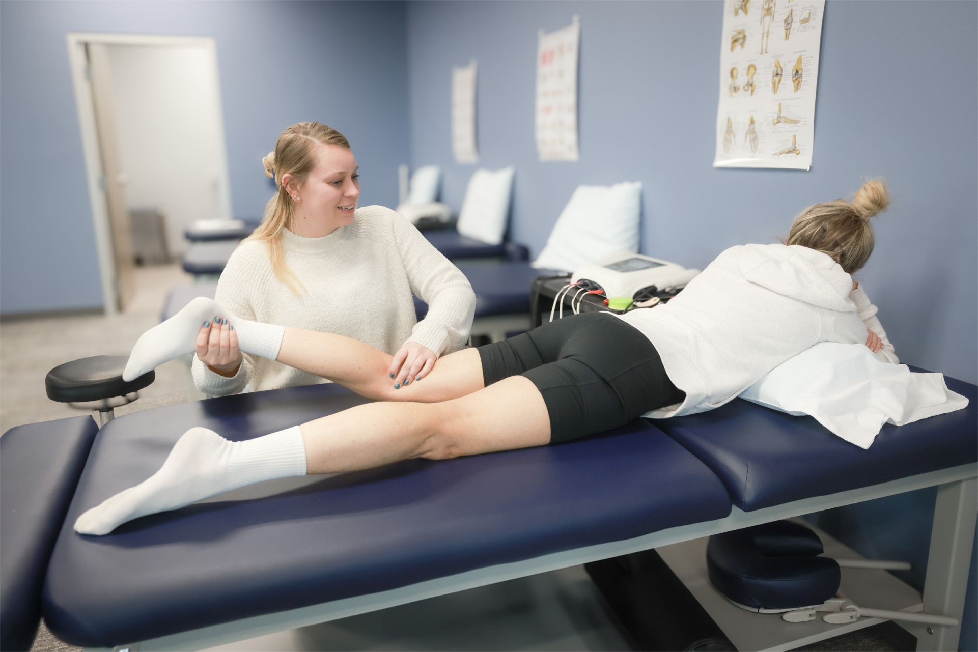 A physical therapist examines a female patient's left leg while the patient is laying down on a physical therapy bed.