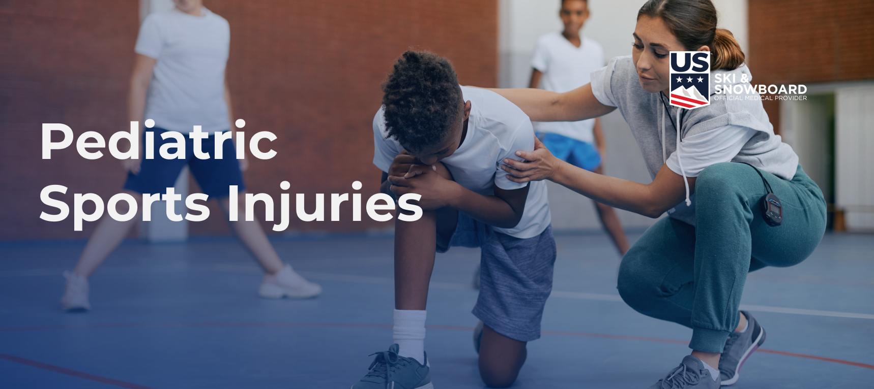 A young boy in a gym clutching his knee in pain while an adult comforts him. Text overlay reads "Pediatric Sports Injuries" with a US Ski & Snowboard logo at the upper right side.